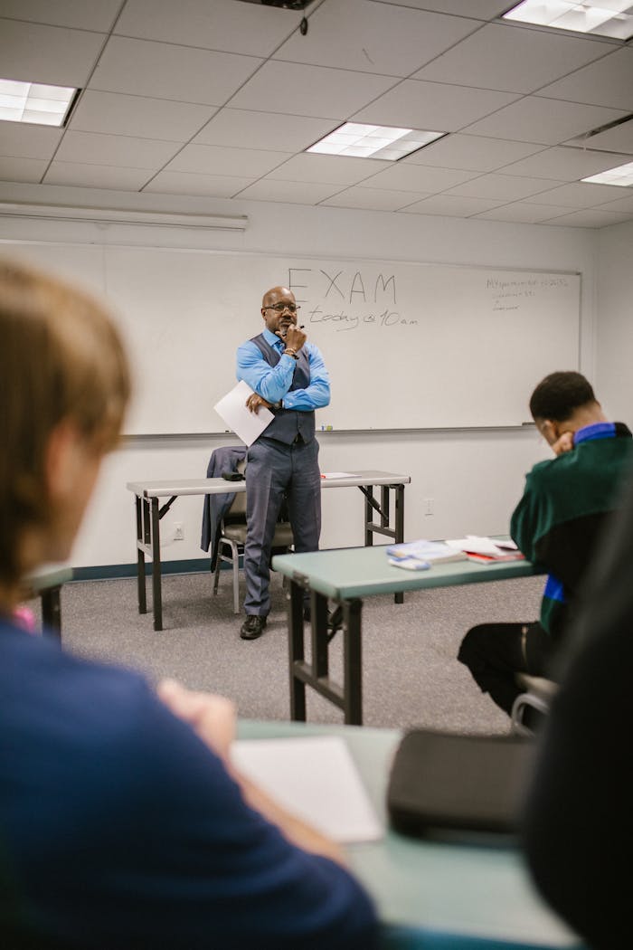 services-img A professor stands attentively in a classroom observing students taking an exam.