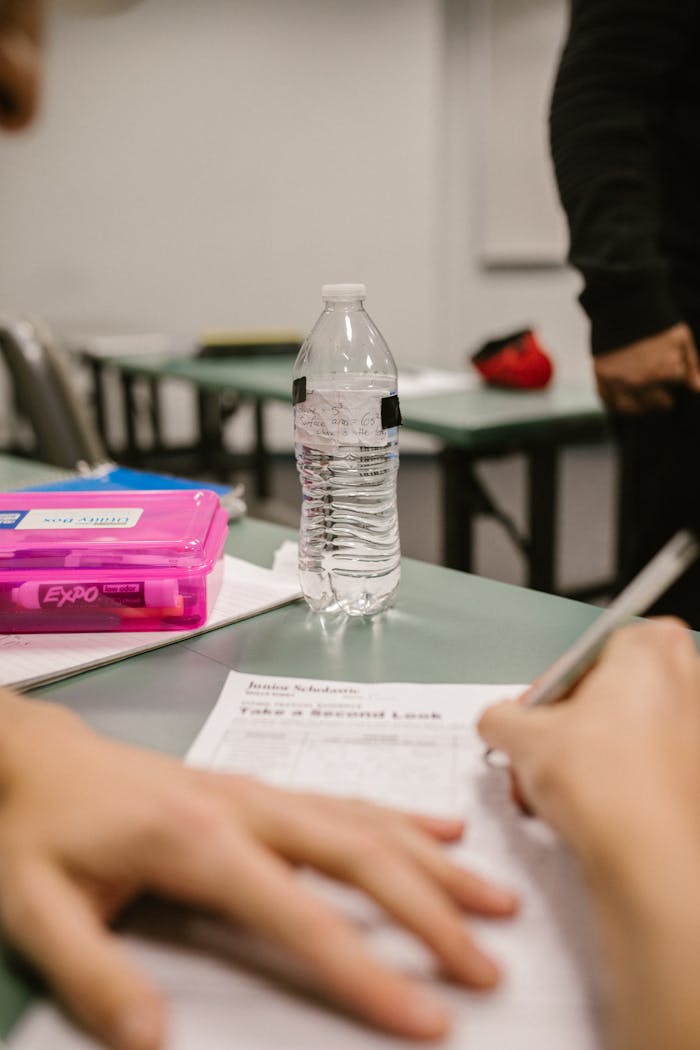 our-services-1 Close-up of a student writing during a test in a classroom setting with a water bottle on the desk.